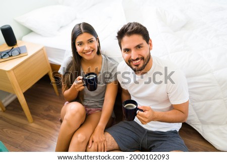 Enjoying a relaxing time in the morning. Attractive couple in pajamas smiling and making eye contact while drinking a hot cup of coffee in the bedroom 