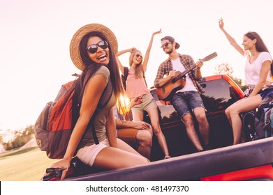 Enjoying Road Trip With Best Friends. Group Of Young Cheerful People Dancing And Playing Guitar While Enjoying Their Road Trip In Pick-up Truck Together 