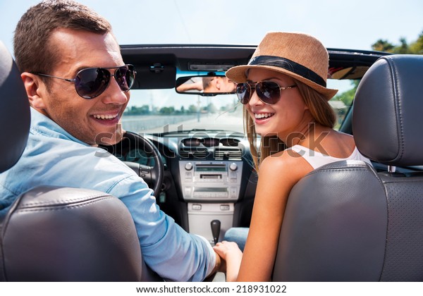 Enjoying road trip together. Beautiful young couple\
enjoying road trip in their convertible and looking over shoulder\
with smile