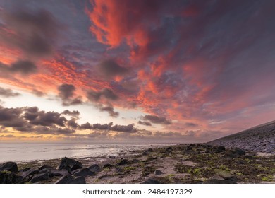 Enjoying a spectacular sunset over the Wadden Sea. The setting sun creates a beautiful red glow in the damp clouds. It is low tide in the Wadden Sea, revealing the seaweed-covered stones. - Powered by Shutterstock