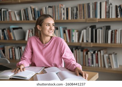 Enjoying study process. Happy inspired young generation z female student distracted from academic work on project at desk look aside from book with smile create new idea satisfied with learning result