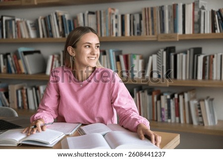 Enjoying study process. Happy inspired young generation z female student distracted from academic work on project at desk look aside from book with smile create new idea satisfied with learning result