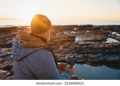 Enjoying the sunset while controlling a drone over rocky shores on a peaceful evening by the ocean - Powered by Shutterstock