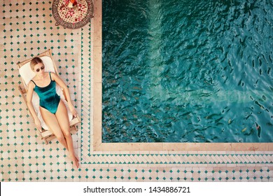 Enjoying suntan. Vacation concept. Top view of young woman on the sun lounger near  the private swimming pool in beautiful moroccan backyard.