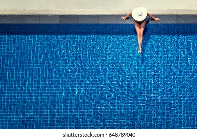 Enjoying suntan. Vacation concept. Top view of slim young woman in hat in the big swimming pool.