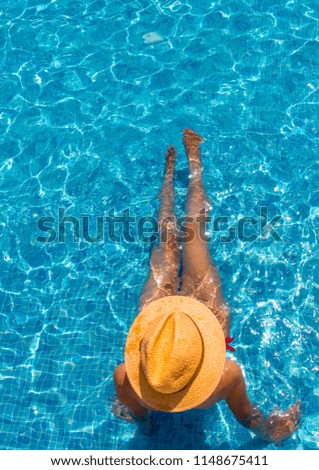 Enjoying suntan. Vacation concept. Top view of slim young woman with a red bikini, a sunhat in a swimming pool. With plenty of copy space.