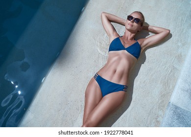 Enjoying suntan and vacation. Top view portrait of pretty young woman in blue swimsuit bikini lying near swimming pool.
