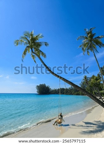 Enjoying a tranquil moment on a sandy beach in Koh Kood, Thailand, while swinging gently from a palm tree. The sun shines bright in a clear blue sky, perfect for relaxation.