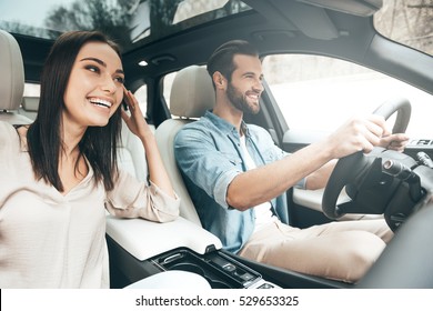 Enjoying travel. Beautiful young couple sitting on the front passenger seats and smiling while handsome man driving a car