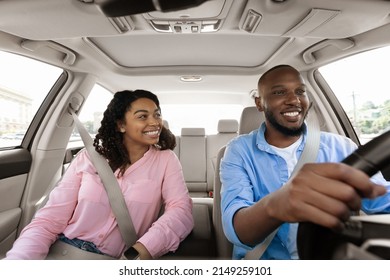 Enjoying Travel Concept. Smiling African American man driving modern luxury car, happy young woman sitting on the front passenger seat, looking on the driver, family going on roadtrip, windshield view - Powered by Shutterstock