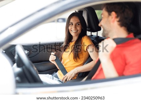 Enjoying travel. Excited happy young couple sitting at front seats and smiling to each other, handsome bearded man driving auto, taking his pretty girlfriend or wife on vacation, car trip