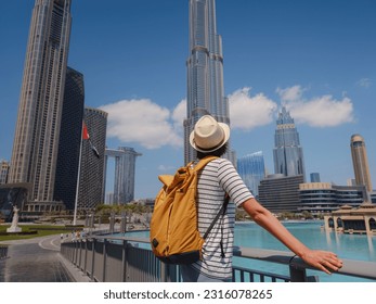 Enjoying travel in United Arabian Emirates. Young woman with yellow backpack walking on Dubai Downtown in sunny summer day. view from the back or rear view