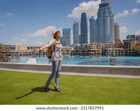 Enjoying travel in United Arabian Emirates. Young woman with yellow backpack walking on Dubai Downtown in sunny summer day.