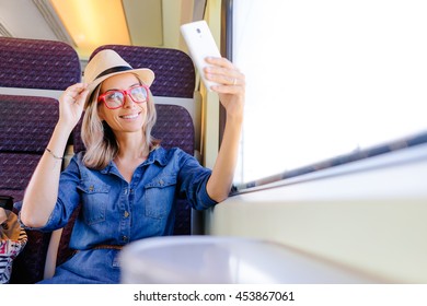 Enjoying Travel. Young Pretty Woman Traveling By The Train Sitting Near The Window Using Smartphone, Taking Selfie.