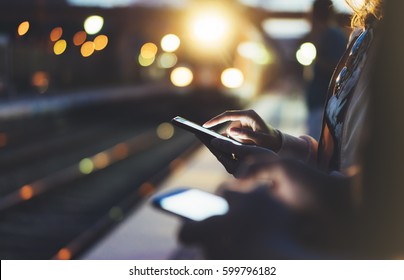 Enjoying Travel. Young Woman Waiting On Station Platform On Background Light Electric Moving Train Using Smart Phone In Night. Tourist Text Message And Plan Route Of Stop Railway, Railroad Transport