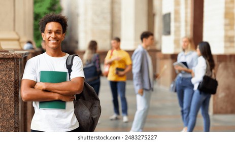 Enjoying university life. African guy holding books and smiling, standing against friends - Powered by Shutterstock