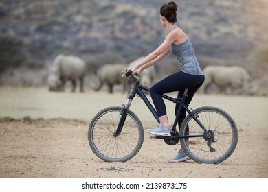 Enjoying untamed Africa. Shot of a young woman on a bicycle looking at a group of rhinos in the veld. - Powered by Shutterstock