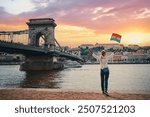 Enjoying vacation in Budapest. Young traveling woman with national hungarian flag walking on riverside promenade with city view on sunset