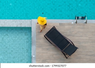 Enjoying vacation concept - Aerial view of Asian woman in yellow dress and summer hat walking around swimming pool near chaise-longue in hotel resort for leisure in vacation. 