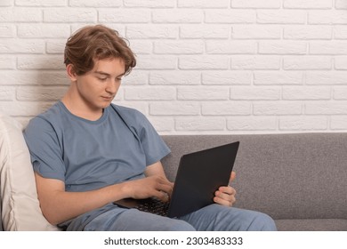 Enjoying Weekend. Handsome teen boy Using laptop While Sitting Leaning On Couch At Home, Happy Guy Relaxing In Living Room, Browsing Internet Or Messaging With Friends, Selective Focus - Powered by Shutterstock