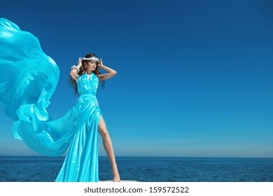 Enjoyment. Fashion Model Woman With Blowing Dress Over Blue Sky, Outdoors. Brunette Girl