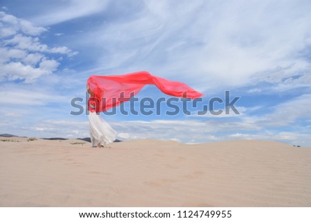 Enjoyment - free, happy and beautiful woman enjoying desert in white dress and large pink scarf in her hands. Embracing freedom with arms outspread in air against the sky. Coral, red color dupatta.