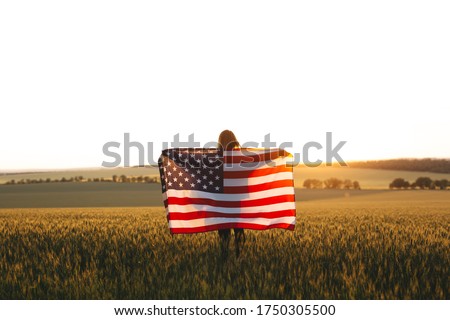 Enjoyng woman with American flag in a wheat field at sunset. 4th of July.  Independence Day, Patriotic holiday.