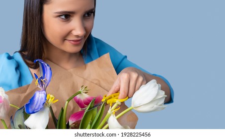 Enlarged Photo Of A Brunette Smiling Looks To The Side Holding A Bouquet Of Tulips In Her Hands And Cuts Off Dull Flowers With Scissors. Blue Neon Background And Space For Ad