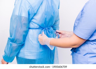 Enlarged Photo Of The Hands Of A Nurse Tie A Disposable Gown To A Patient Preparing For Hospitalization.