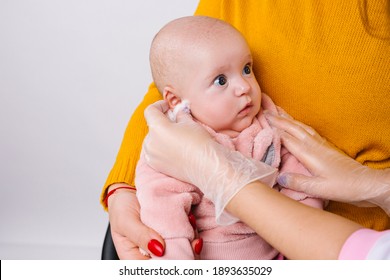 Enlarged Photo Of A Little Cute Baby Girl Whose Doctor's Hands Rub Her Ear In Preparation For The Ear Piercing, Beauty Procedure.