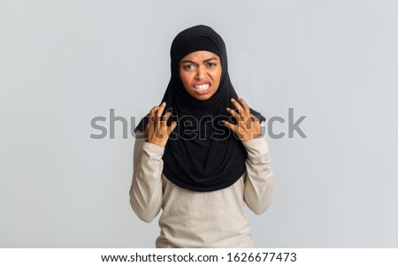 Enough. Annoyed black muslim woman in hijab emotionally gesturing with hands and grimacing full of fury, standing over gray background, free space