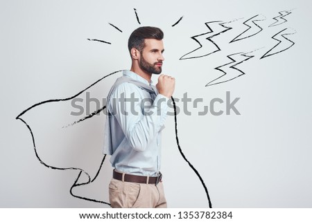 I am enough strong! Confident and attractive young man wearing a drawn cape showing gesture of success while standing against grey background with illustration of the lightning bolts