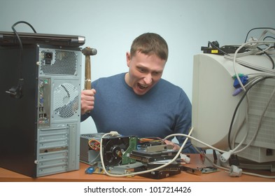 Enraged computer technician man is screaming and breaks a PC by hammer. PC repair service center. Mad system administrator in stress overburdened by work.