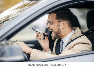 An enraged young elegant executive is driving his car while leaving an angry voice message on the phone. - Shutterstock ID 2366206427