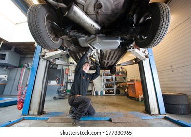 ENSCHEDE, NETHERLANDS - DEC 13: A Mechanic Is Checking The Exhaust Of A Car Who Is Lifted Up In A Repair Service Station, December 13, 2013 In The Netherlands