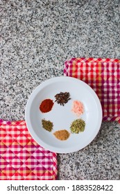 Ensemble Of Spices In A White Dish Over A Granite Countertop. Top Down View.