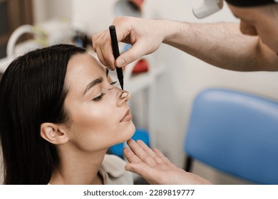 ENT doctor is drawing mark up lines on nose before rhinoplasty surgery. Rhinoplasty markup. Rhinoplasty is reshaping nose surgery for change appearance of the nose and improve breathing - Shutterstock ID 2289819777