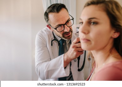 ENT physician looking into female patient's ear with an instrument. Male doctor examining patient's ear with otoscope in his clinic. - Powered by Shutterstock