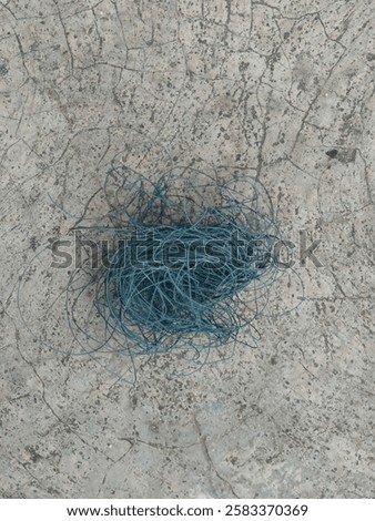 Entangled blue thread, set against a backdrop of concrete floor plaster, close up photograph of the twisted plastic thread, an isolated object image