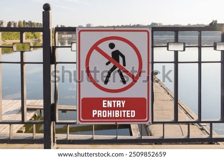 Enter Forbidden - a simple white and red warning sign on a black metal fence, with a lake in the background.