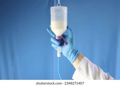 Enteral nutrition diet bottle hanging and infusing enteral diet throughout an infusion set. Professional holding and checking the diet. Blue background  - Shutterstock ID 2348271407