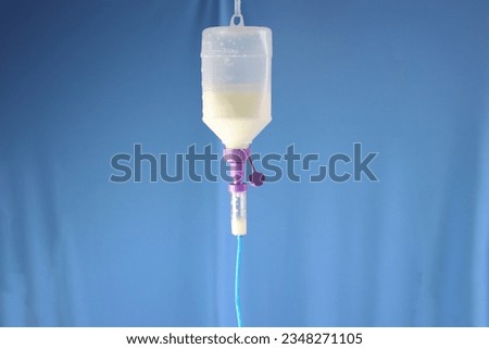 Enteral nutrition diet bottle hanging and infusing enteral diet throughout an infusion set. Blue background 