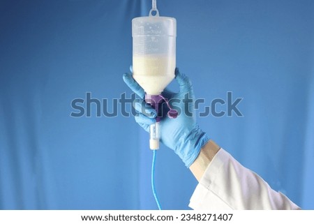Enteral nutrition diet bottle hanging and infusing enteral diet throughout an infusion set. Professional holding and checking the diet. Blue background 