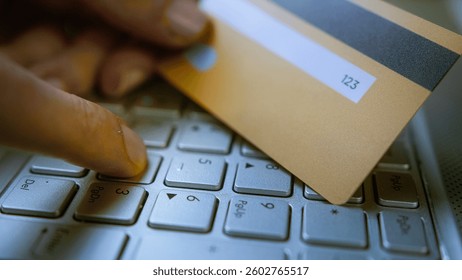 Entering CVVCVC code on a laptop keyboard with a credit card in hand, online payment security, cyber fraud risk, digital transactions, e-commerce safety