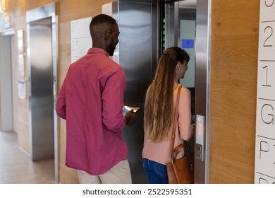 Entering elevator, man holding smartphone and woman pressing button, office setting. Business, corporate, technology, colleagues, professional, convenience - Powered by Shutterstock