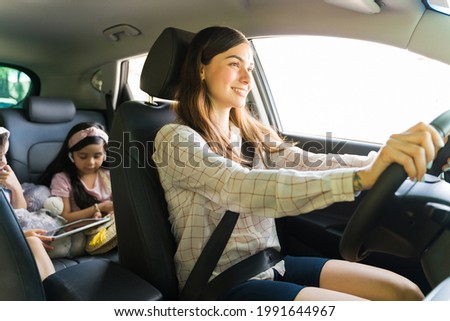 Entertaining my children. Beautiful young mom smiling while driving a car with her kids in the back watching a movie on a tablet with headphones during her errands
