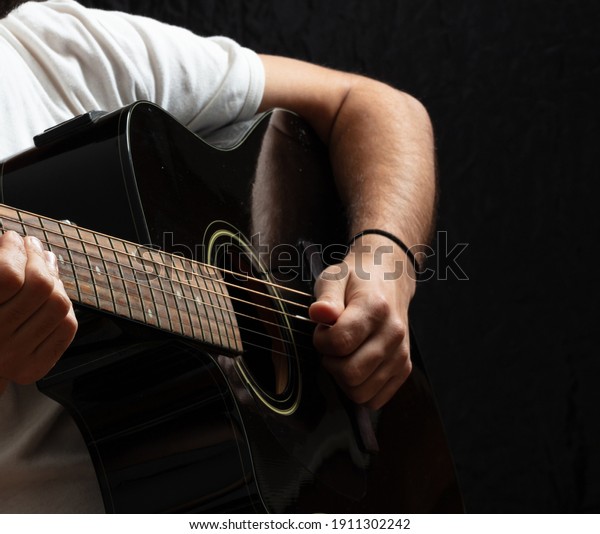 Entertainment concept. Young man playing acoustic\
guitar, dark background. Guitarist in casual white shirt holds\
electric black instrument at\
studio.