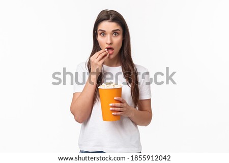 Entertainment, fun and holidays concept. Portrait of woman entertained, watching movie with interest, enjoying favorite tv series, eating popcorn and staring camera, stand white background