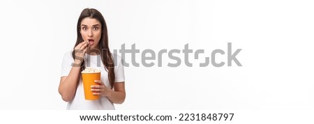 Entertainment, fun and holidays concept. Portrait of woman entertained, watching movie with interest, enjoying favorite tv series, eating popcorn and staring camera, stand white background.