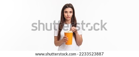 Entertainment, fun and holidays concept. Portrait of skeptical serious-looking young woman watching horror movie and being unimpressed, eating popcorn look camera reluctant.